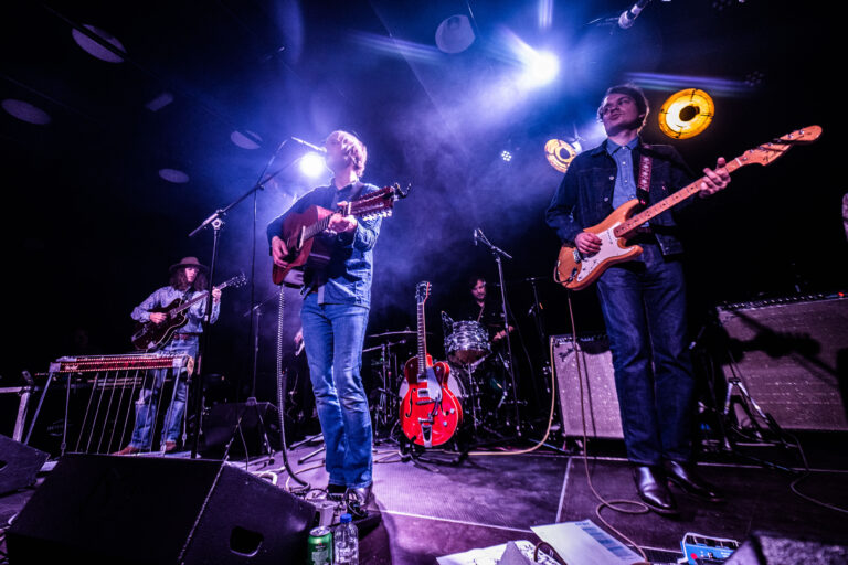Een band speelt live muziek op een podium met kleurrijke lichten.
