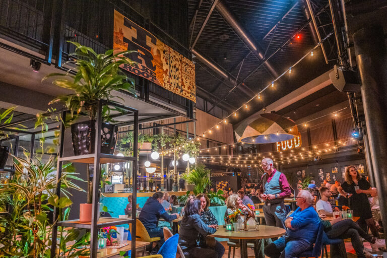 Een sfeervol restaurant met planten, een kleurrijke inrichting en gasten aan de tafels, verlicht door sfeerverlichting.