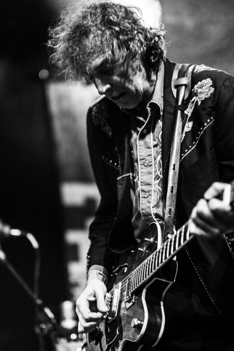Een muzikant speelt gitaar op een podium in zwart-wit.