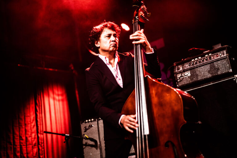 Een man in een zwart pak speelt contrabas op een podium met rode verlichting.