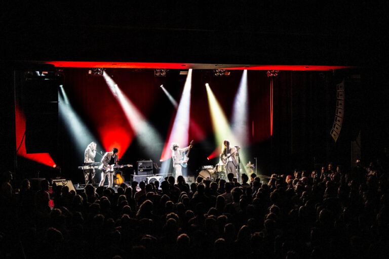 Een energieke liveband speelt op een podium met opvallende verlichting voor een enthousiast publiek.