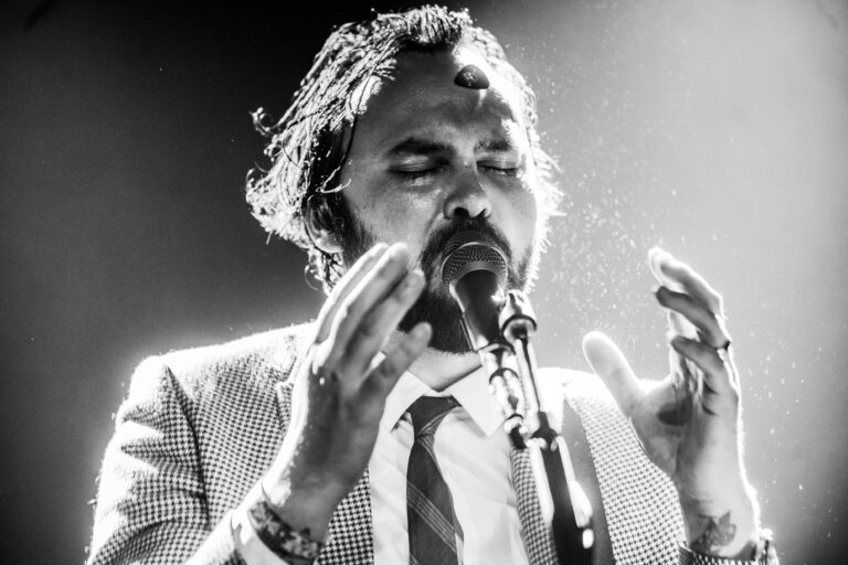 Een zwart-witfoto van een zanger die gepassioneerd een microfoon vasthoudt en zijn handen gebruikt om zijn emotie over te brengen.