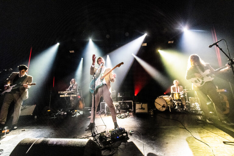 Een band speelt live op het podium met kleurrijke verlichting en verschillende instrumenten.