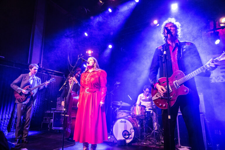 Een band speelt live op het podium met een zangeres in een rode jurk en muzikanten op verschillende instrumenten.
