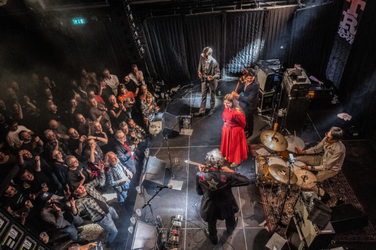 Een live muziekoptreden met een zangeres in een rode jurk en muzikanten op het podium, omringd door een enthousiast publiek.