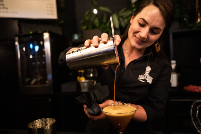Een bartender giet een cocktail uit een shaker in een glas.