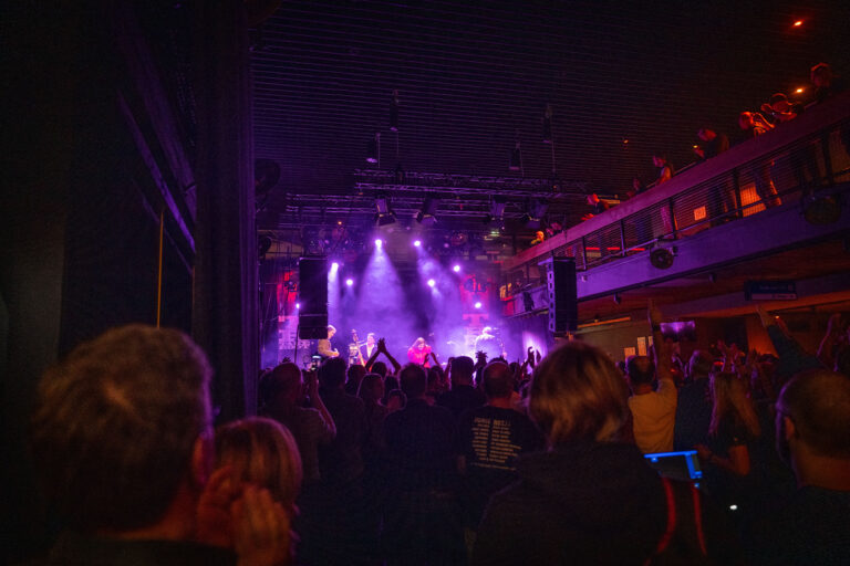 A crowded concert scene with colorful stage lights illuminating performers.