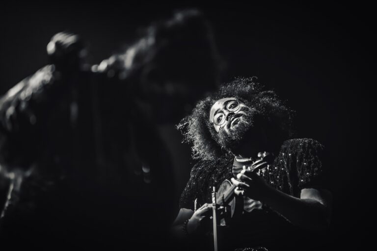 Zwart-wit foto van een muzikant met een bushy kapsel die intens aan een instrument speelt.