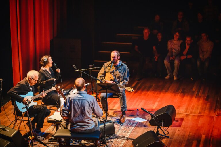Drie muzikanten spelen samen op het podium voor een publiek in een intieme setting.