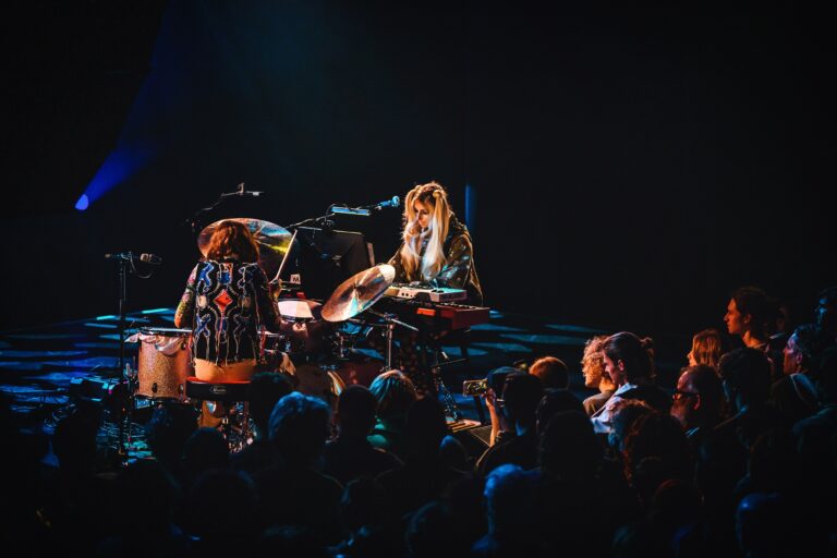 Twee muzikanten optreden op het podium voor een donker publiek.