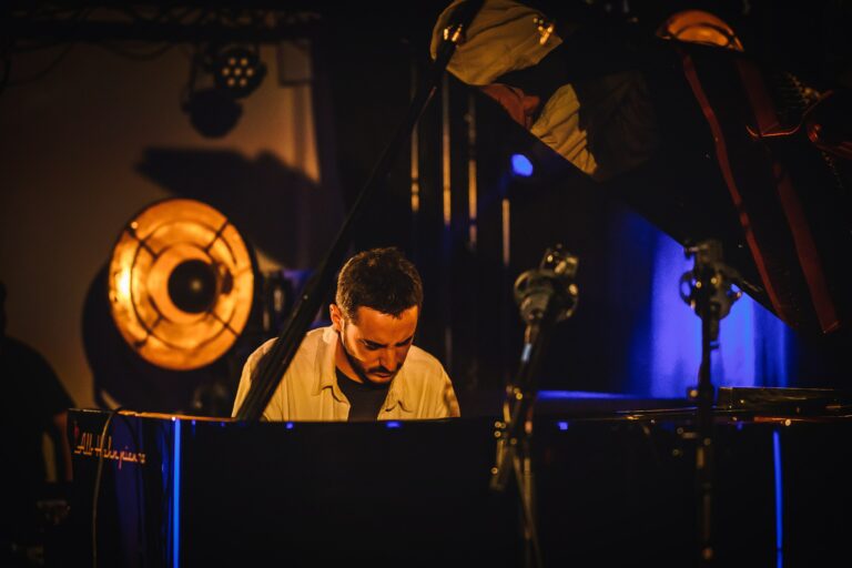 Een muzikant speelt op een piano in een sfeervolle, verlichte omgeving.
