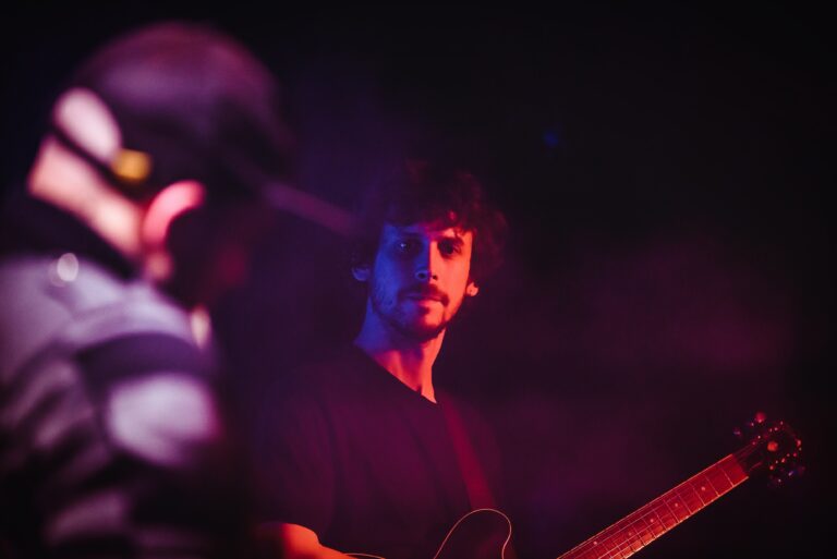 Een muzikant speelt een gitaar op een sfeervol verlichte podium met nevel.