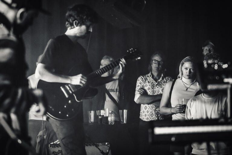 Een muzikant speelt gitaar op een podium, terwijl het publiek aandachtig kijkt.