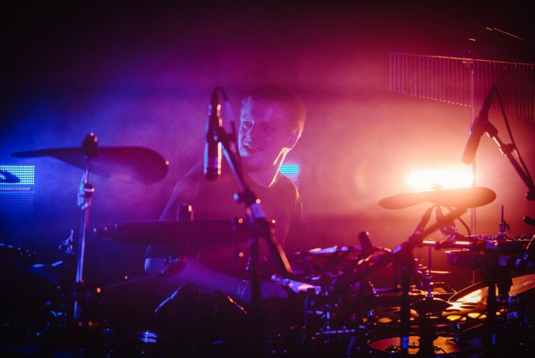 Een drummer speelt in een sfeervolle setting met kleurrijke lichten en mist.