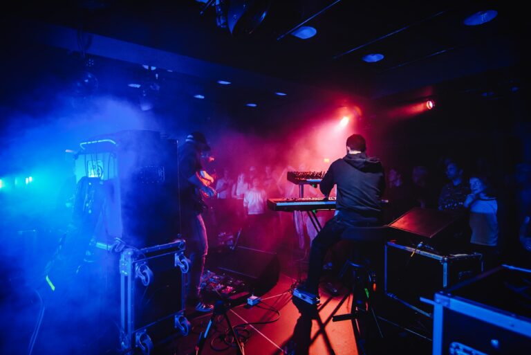 Een muzikant speelt keyboard op een podium met kleurrijke verlichting en een enthousiast publiek op de achtergrond.