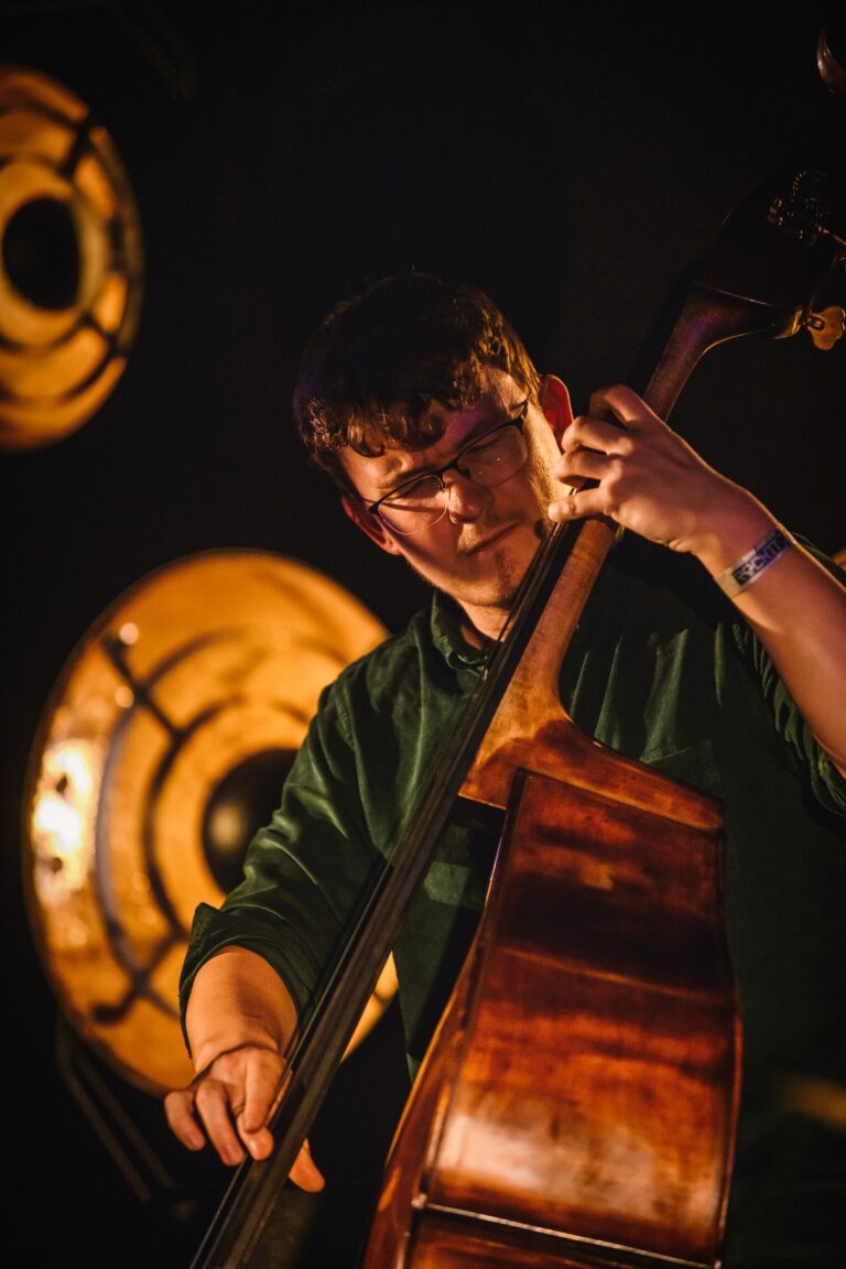 Een muzikant speelt een contrabas op een podium met op de achtergrond grote, ronde verlichtingselementen.