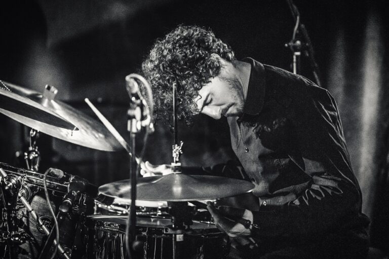 Een drummer is geconcentreerd bezig met het bespelen van zijn drums op een podium.