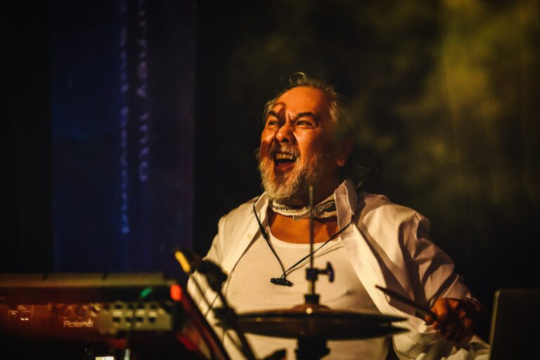 Een drummer met een glimlach speelt enthousiast op het podium met zijn drumstel.