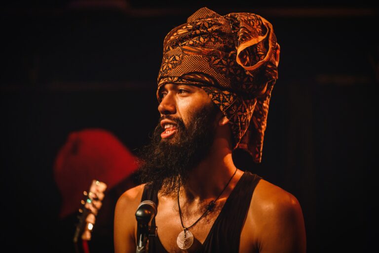 Een man met een opvallende hoofdband en baard zingt in een sfeervolle muzieksetting.