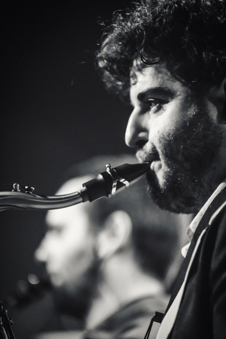 Een muzikant die een saxofon speelde, met een andere muzikant op de achtergrond.