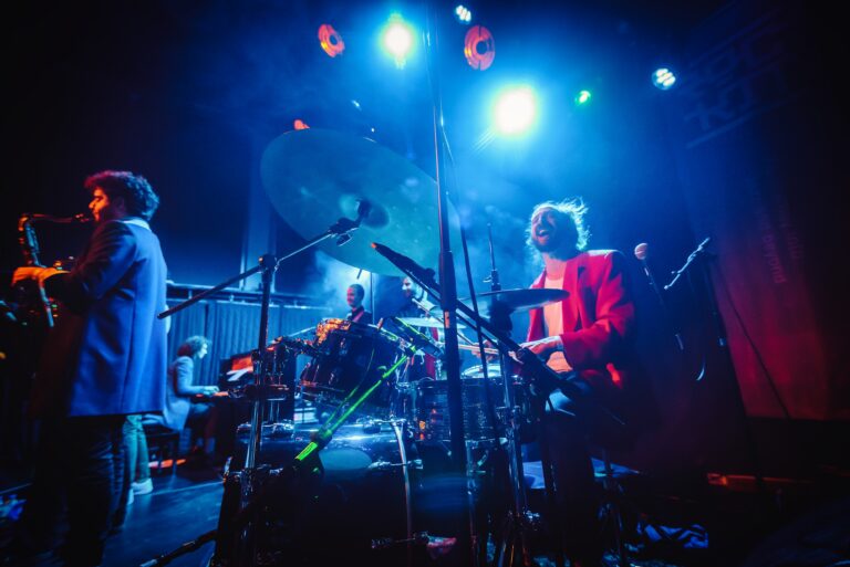 Een live band speelt op het podium onder kleurrijke verlichting.