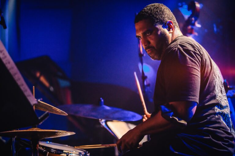 Een drummer in actie achter zijn drumstel met een blue-achtige lichtsetting.