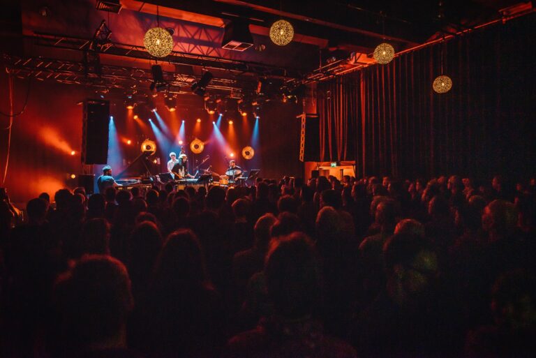 Een druk bezocht concert met kleurrijke verlichting en een muzikale act op het podium.