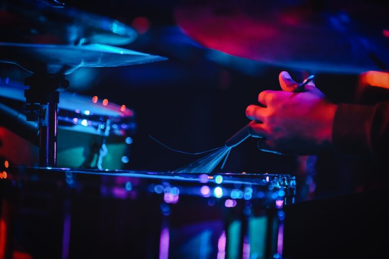 Een close-up van een hand die een drum bespeelt, omgeven door kleurrijke verlichting.