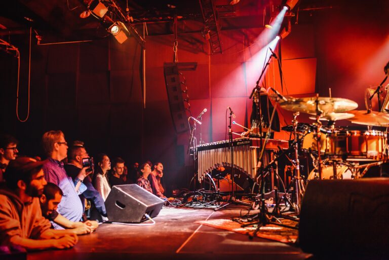 Een muzikant speelt op een podium terwijl het publiek in het donker toekijkt, verlicht door een enkele lichtstraal.