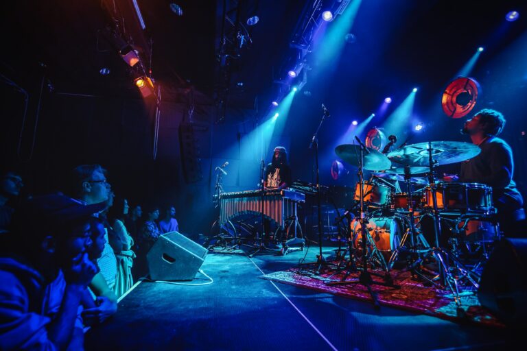 Een liveband speelt op een podium, omringd door kleurrijke lichteffecten en een publiek dat geniet van de muziek.