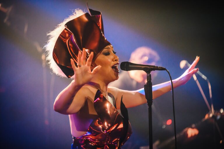 Zangeres met een opvallende koptelefoon maakt een krachtige zanggebaar op het podium.