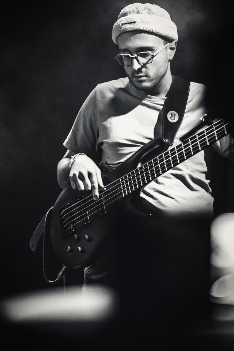 Een muzikant speelt basgitaar op een podium in zwart-wit.