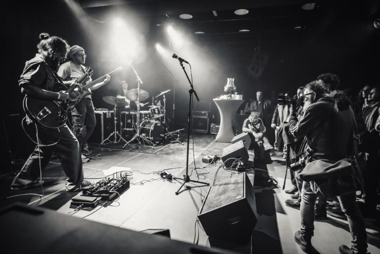 Een live band speelt op een podium, terwijl het publiek naar de muziek luistert.