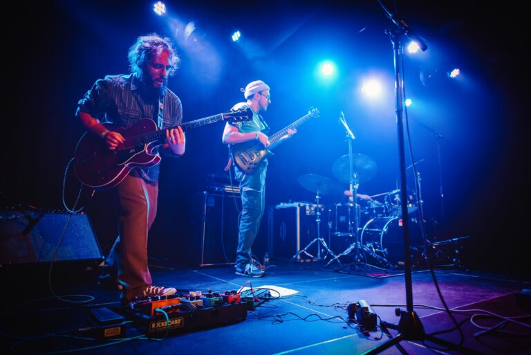 Een band speelt live op het podium met kleurrijke spotlights en diverse muziekinstrumenten.