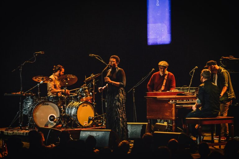 Een band speelt live op het podium met een zangeres en muzikanten op verschillende instrumenten.