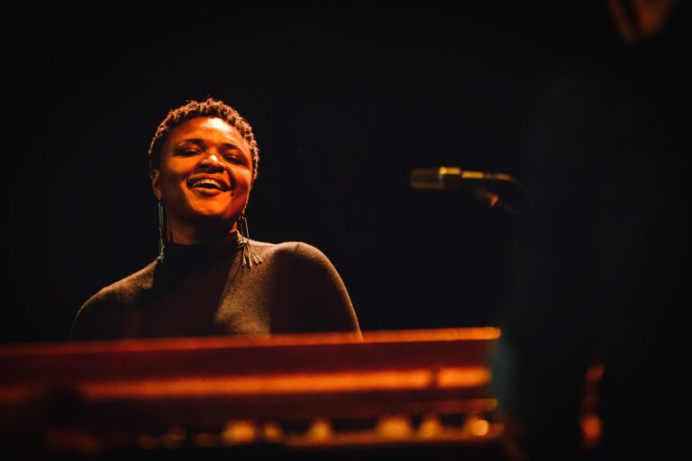 Een muzikant met een brede glimlach speelt op een keyboard op het podium.