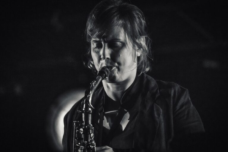 Een muzikant speelt saxofon in een low-key, zwart-wit setting.