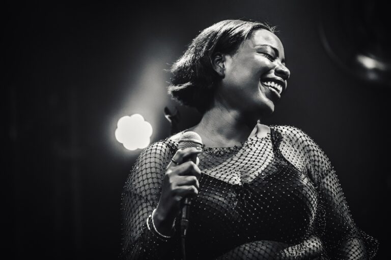 Een zangeres met een glimlach houdt een microfoon vast terwijl ze optreedt op een podium.