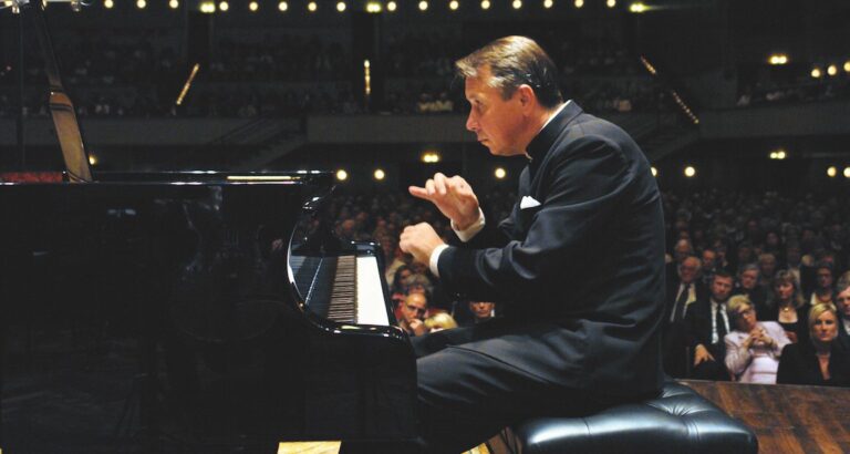 Pianist die geconcentreerd aan het spelen is op een vleugelpiano, met een publiek op de achtergrond.