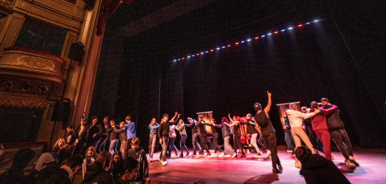 Een polonaise van grote groep jongeren op het podium van De Stadsschouwburg.