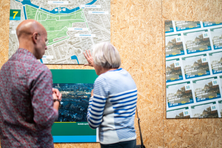 Opening informatiecentrum stationsgebied - bewoner en projectontwikkelaar staan voor muur met plattegrond en krijgt uitleg