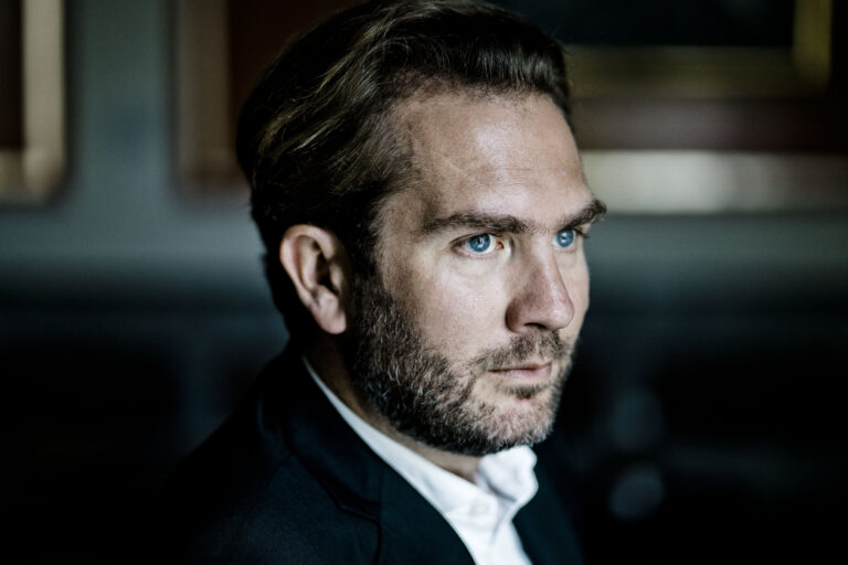 Close-up foto van Thomas Oliemans in pak die wegkijkt van de camera.