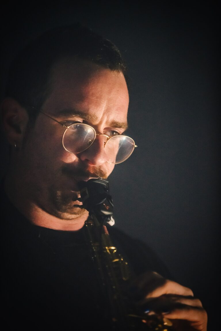 Een man speelt saxofon in een donkere omgeving.