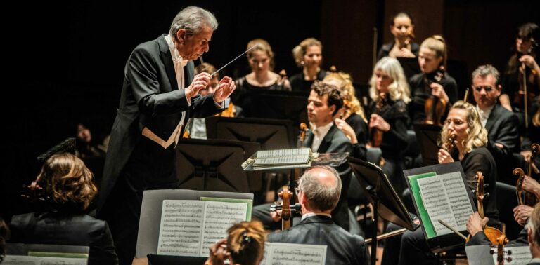 Dirigent Hartmut Haenchen tussen de orkest leden.