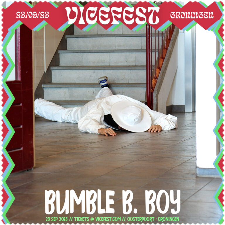 Een persoon in een witte outfit ligt op de grond vlakbij een trap in een binnenruimte.