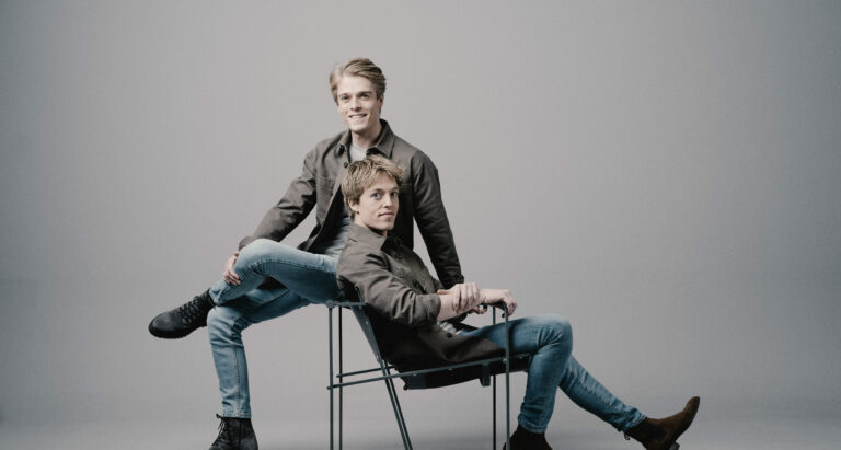 Broertjes Jussen poseren zittend op 2 stoelen met een taupe achtergrond.