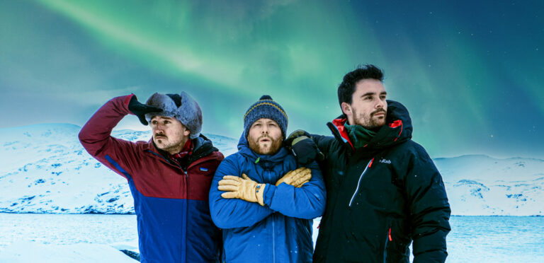 Bas, Chris en Domien (drie mannen) gekleed in winterse kleren staan in de sneeuw te kijken naar het Noorderlicht