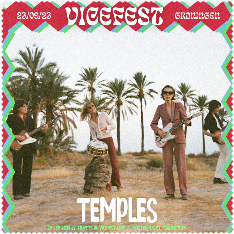 Een band speelt muziek in een woestijnachtige omgeving met palmbomen op de achtergrond.