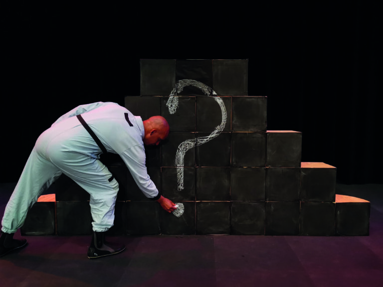 Acteur schrijft vraagteken op stapel dozen