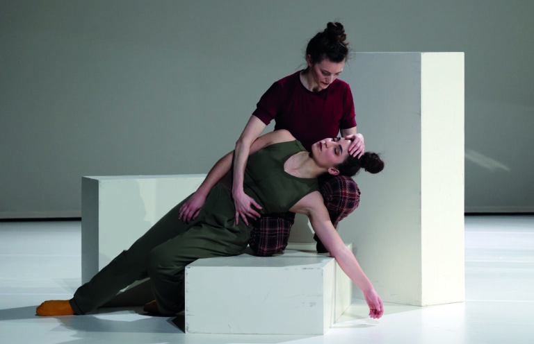 Twee vrouwelijke dansers in een artistieke pose, waarbij één danseres licht achterover leunt op een andere.